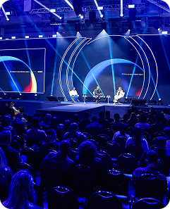 Palestrantes no Palco Connect. O palco é cheio de luzes azuis e possui um grande telão.